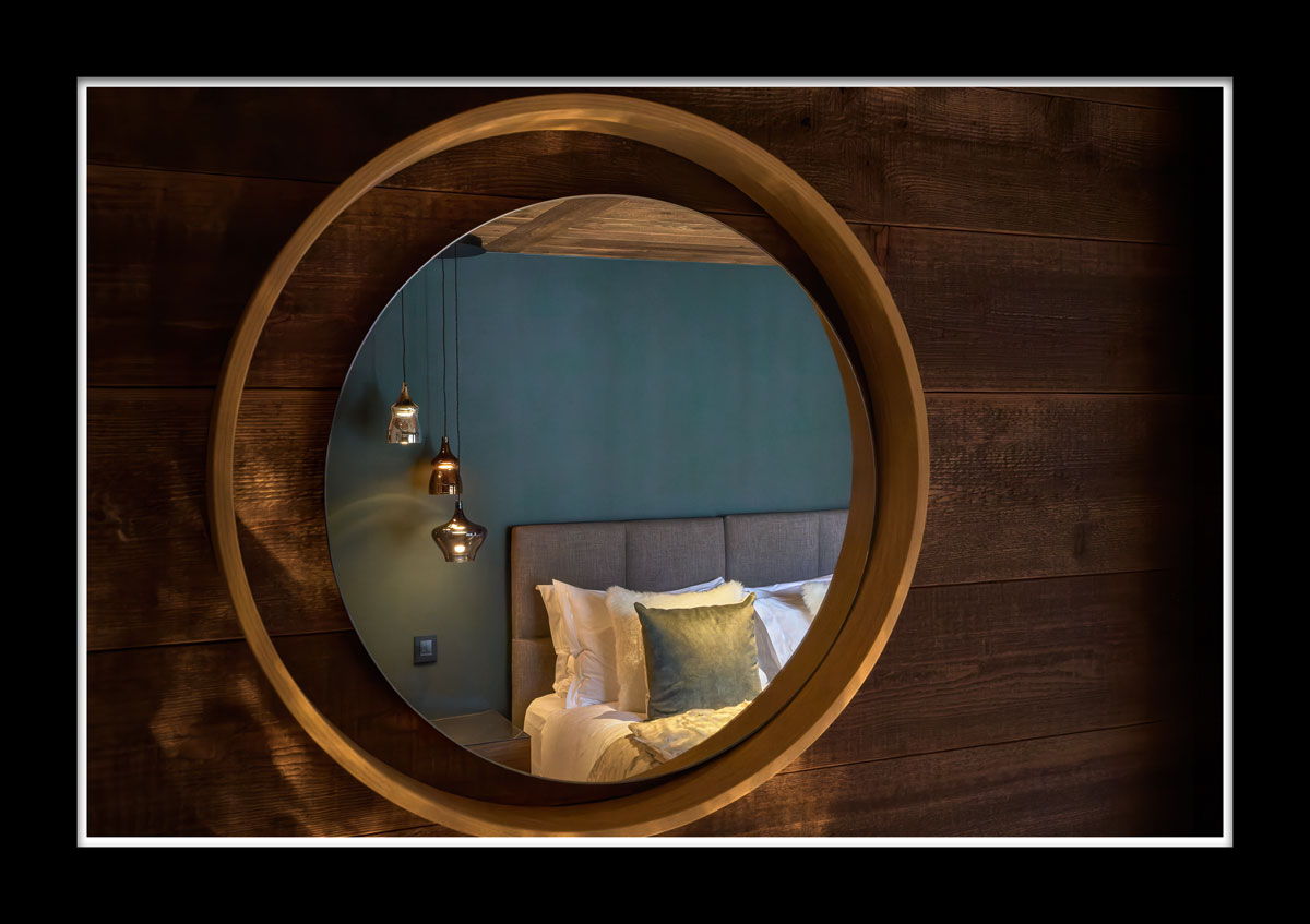 Photographie immobilier de prestige : miroir rond en bois reflétant une chambre de chalet